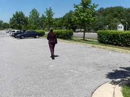4 photos show Dona stepping off a curb in the parking lot and walking across about 7 parking spaces, then standing at one of the lane markers for the parking spaces.