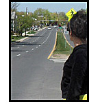 photo shows a woman looking at two vehicles approaching from about a block away on a 3-lane road.